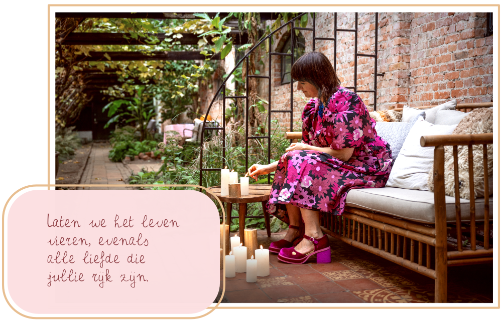 Tolk van Hartzaken Linda Blij zit op een bankje in romantische setting. Zij draagt een kleurige jurk met roze bloemen. Voor haar staan een aantal witte en goudkleurige kaarsen. Ze heeft een glimlach op haar gezicht en steekt een van de kaarsen aan.